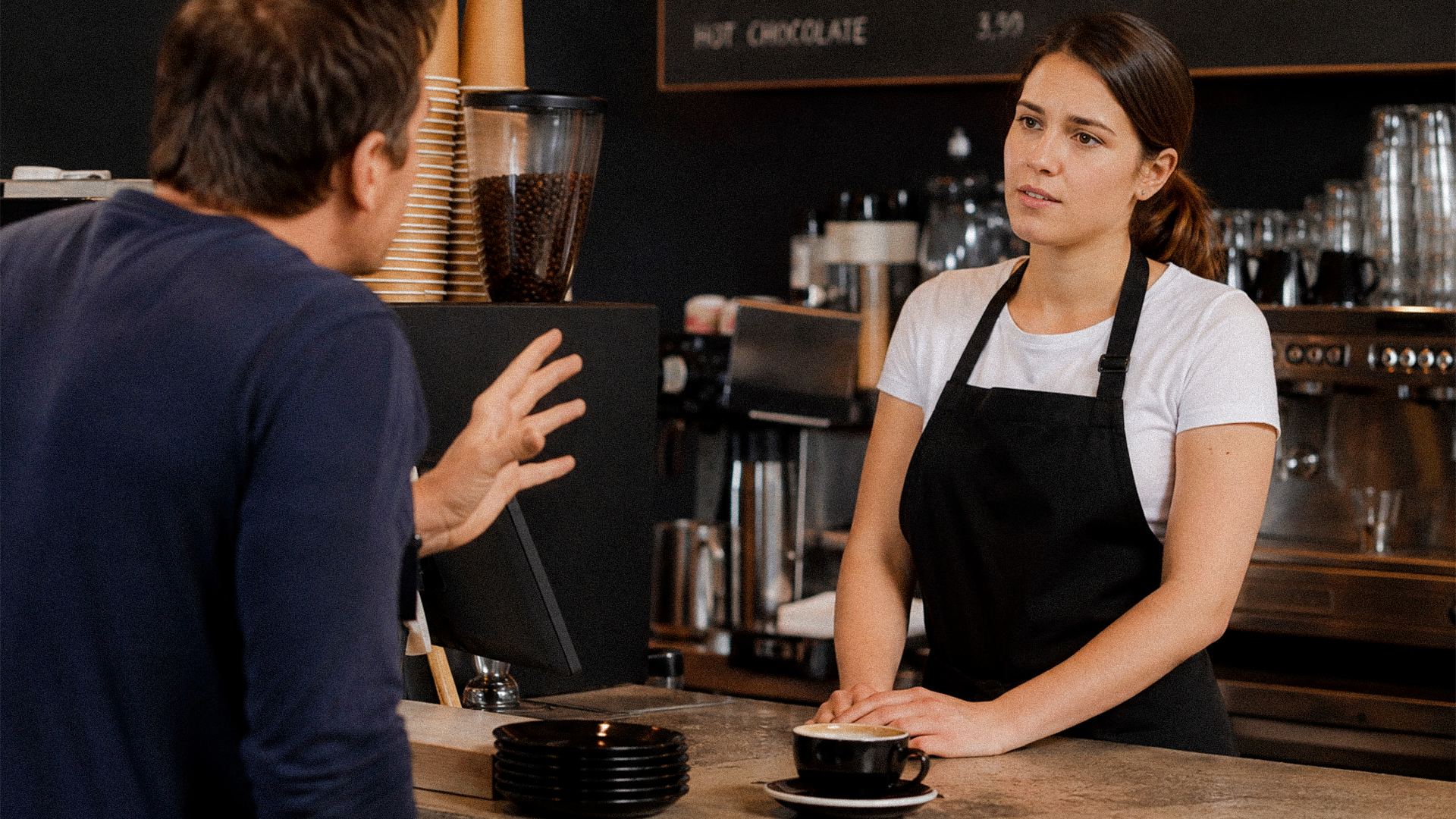 Hospitality worker standing calmly at a counter, illustrating the debate over the customer is always right